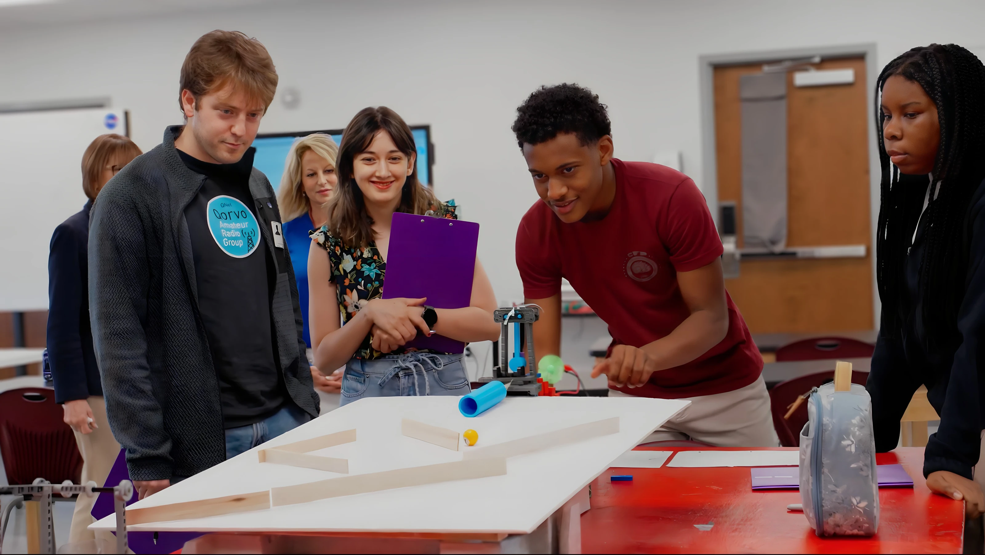 A visiting engineer and students watching a student demonstrate an engineering project